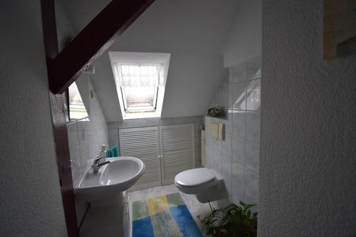 Kleines Badezimmer im Dachgeschoss mit Dachfenster, weißem Waschbecken, Toilette und Fliesen.