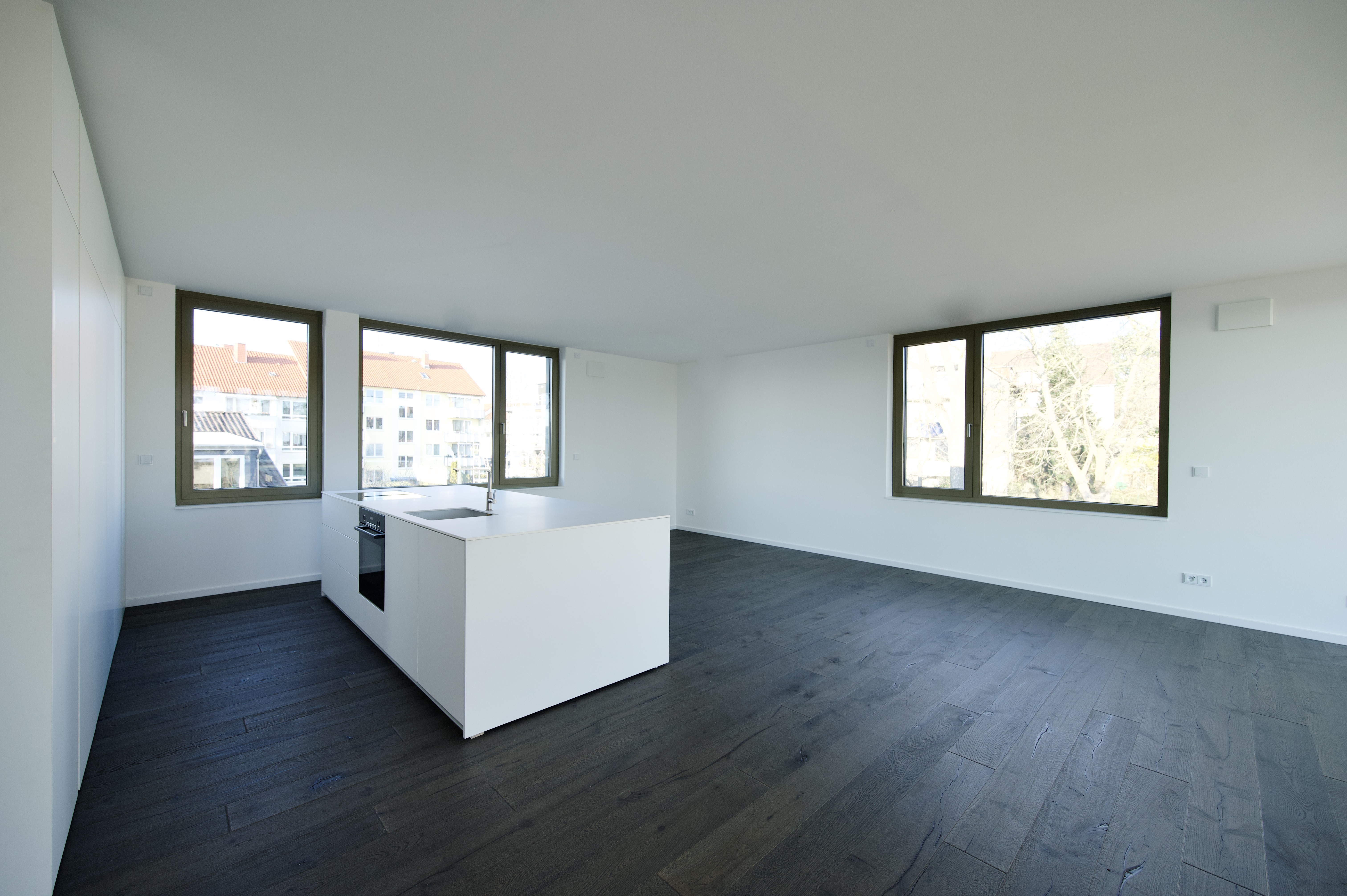 Projekt Himmelsruh – offener Wohnbereich mit dunklem Holzboden und weißer Kücheninsel