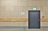 Graue Tür in einer beigen Ziegelwand mit Leuchtschild "Ausgang" und rotem Feuermelder.