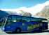Blauer Reisebus "HÜBNER" mit Sternenmuster vor schneebedeckten Bergen.