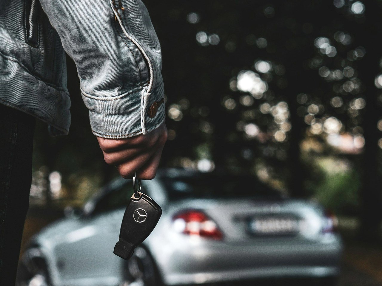 Autoschlüssel in der Hand vor einem silbernen Pkw