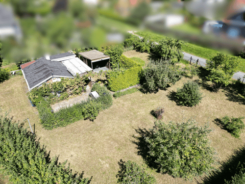Ein Haus mit einem dunklen Dach, umgeben von einem großen grünen Garten und Bäumen.