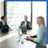 Drei Personen in Anzügen sitzen an einem Konferenztisch mit Laptops und diskutieren.