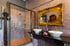 Badezimmer mit braunen Fliesen, begehbarer Dusche, zwei Waschbecken und einem opulenten goldenen Spiegel.
