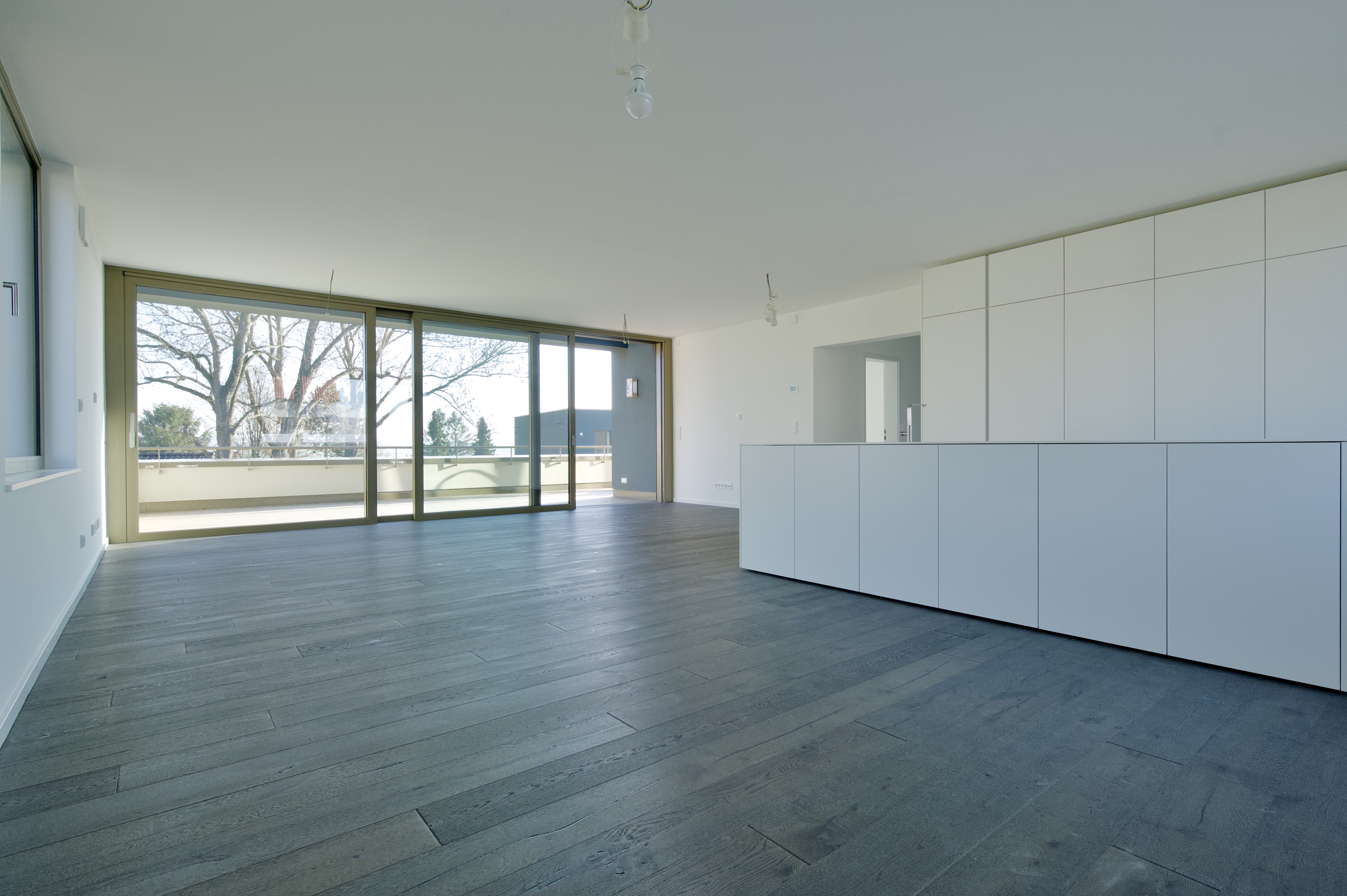 Projekt Himmelsruh – heller Wohnraum mit dunklem Holzboden, weißer Einbauküche und großer Fensterfront