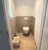 Eine Toilette mit grauen Fliesen und weißer Wand, ein kleines Waschbecken auf dem Boden.