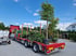 Roter Lastwagen mit Anhänger, beladen mit Topfpflanzen und einem großen Baum, auf einem Parkplatz.
