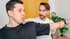 Ein Mann in einem schwarzen T-Shirt mit einem Physiotherapeuten, der seinen Arm hält und seine Schulter berührt.