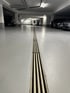 Eine Entwässerungsrinne in einem hellgrauen Parkhaus mit geparkten Autos an beiden Seiten.