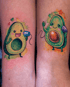 Zwei bunte Avocado-Tattoos auf Unterarmen, die über ein Dosentelefon miteinander verbunden sind und lächeln.