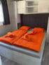 Zwei Betten mit leuchtend orangefarbener Bettwäsche und aufgerollten Handtüchern in einem Schlafzimmer im Mobilehome Villa Aperol.
