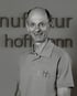 Ein lächelnder Mann in einem Polo-Shirt mit "k.hh"-Logo, vor einer Wand mit dem Wort "hoffmann".