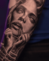 Detailreiches Schwarz-Grau-Tattoo eines Frauengesichts mit weißen Augen, die ein Seil im Mund hält und gefesselte Hände hat.