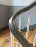 Graues Treppengeländer mit weißen, gedrehten Holzbalustern und hellbraunem Parkettboden.