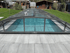 Überdachter Swimmingpool mit dunkelgrauem Rahmen und transparentem Dach in einem Garten.
