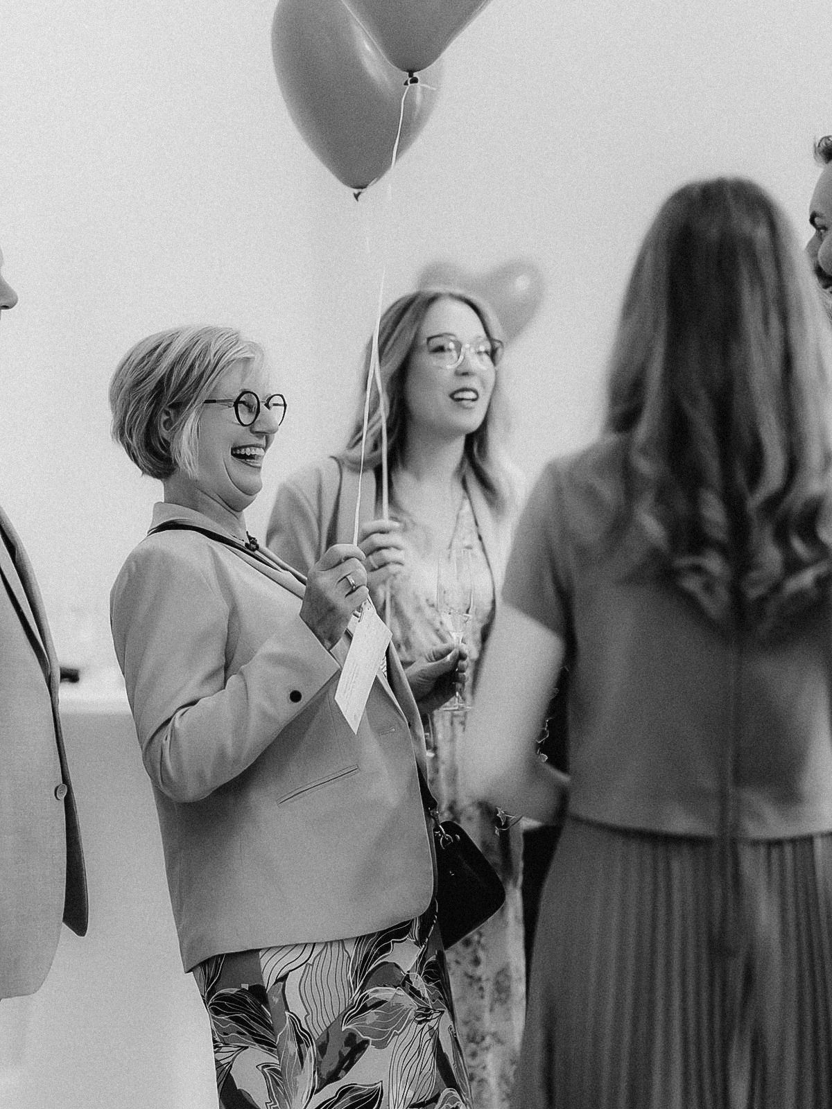 Hochzeitsgäste lachen mit Herzluftballons beim Empfang im Schloss Eller in Düsseldorf.