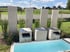 Moderner Gartenbrunnen aus Beton mit Wasserfällen, rechteckigem Becken und hohen Stelen vor einer grünen Landschaft.