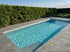 Rechteckiger Pool mit blauem Wasser, umgeben von grauen Fliesen und einer grünen Hecke.
