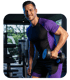 Ein lächelnder Mann in Lila-Schwarz-Sportkleidung hält eine Hantel in einem Fitnessstudio.