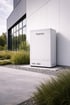 Weißer Fuenseo Batteriespeicher steht außen an einer modernen Hauswand mit Fenstern, umgeben von Kies und grünen Pflanzen.