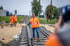 Ein Mann in oranger Arbeitskleidung und Kappe steht auf einem neuen Eisenbahngleis und hält eine Fackel.