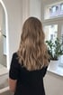 Rückenansicht einer Frau mit langen, gewellten, blonden Haaren in einem Friseursalon.