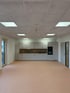 Moderne, helle Teeküche in einem Büro mit grauen Fronten, Holz-Rückwand und quadratischen Deckenleuchten.