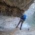 Eine Person im Neoprenanzug seilt sich an einem Wasserfall in einer Schlucht ab.