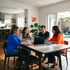 A family and a professional sit at a dining table looking at a laptop and documents in a bright, modern home.