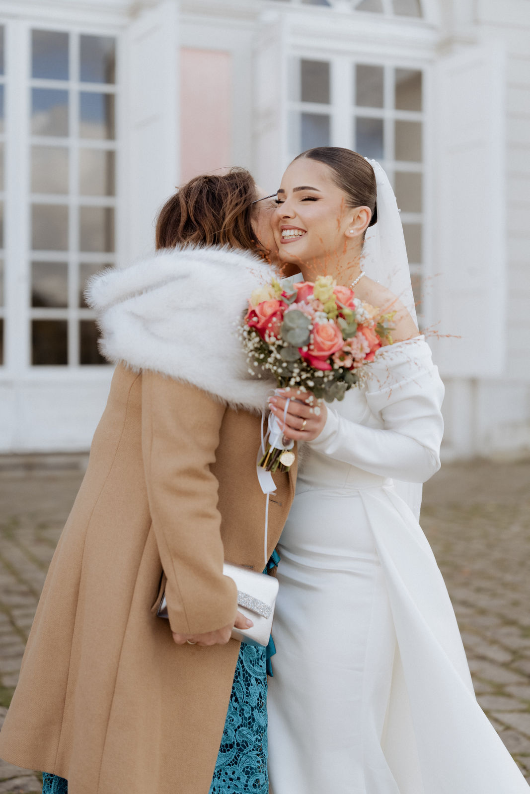 Strahlende Braut umarmt einen Gast beim Empfang vor Schloss Benrath in Düsseldorf.