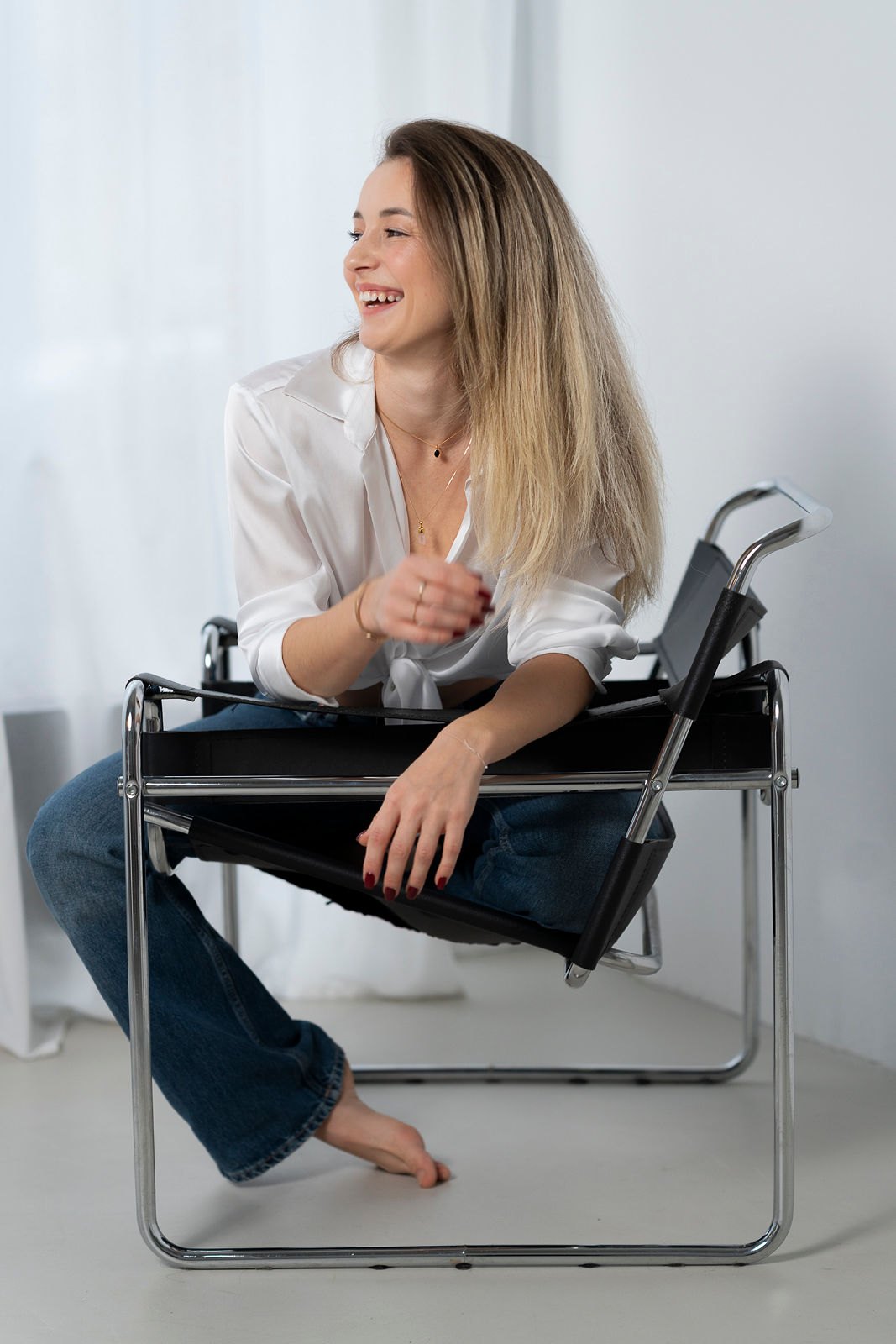Tatjana Schäfer sitzt lachend in weißer Bluse auf einem Lederstuhl
