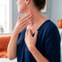 A woman touches her throat and chest with her hands, showing red, irritated skin on her neck.