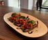 Drei Bruschetta-Stücke mit gewürfelten Tomaten, Basilikum und Balsamico-Glasur auf einem Teller.