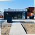 Automaten-Kiosk "SNACK FLASH 24/7" mit Glasfront, Gehweg, Kies und Parkplatz.