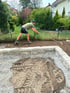 Ein Mann in Arbeitskleidung ebnet mit einer Harke dunkle Erde hinter einer niedrigen Natursteinmauer im Garten.