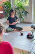 Frau im Schneidersitz auf einer Yogamatte meditiert mit den Händen auf dem Bauch vor einer Klangschale und Kerze.