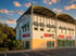 Modernes Bürogebäude mit gewölbtem Dach, TÜV-Schild und Parkplatz unter blauem Himmel bei Sonnenuntergang.