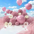 Rosa flauschige Kugeln, glänzende Kugeln, Blumen und Ballons unter blauem Himmel mit weißen Wolken.