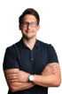 Mann mit Brille, dunkelblauem Poloshirt und verschränkten Armen lächelt.