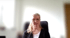 Frau mit Brille und blonden Haaren sitzt vor hellem Hintergrund.