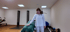 Eine Physiotherapeutin legt ihre Hand auf den Rücken eines Patienten, der auf einer Trainingsbank im Fitnessraum liegt.