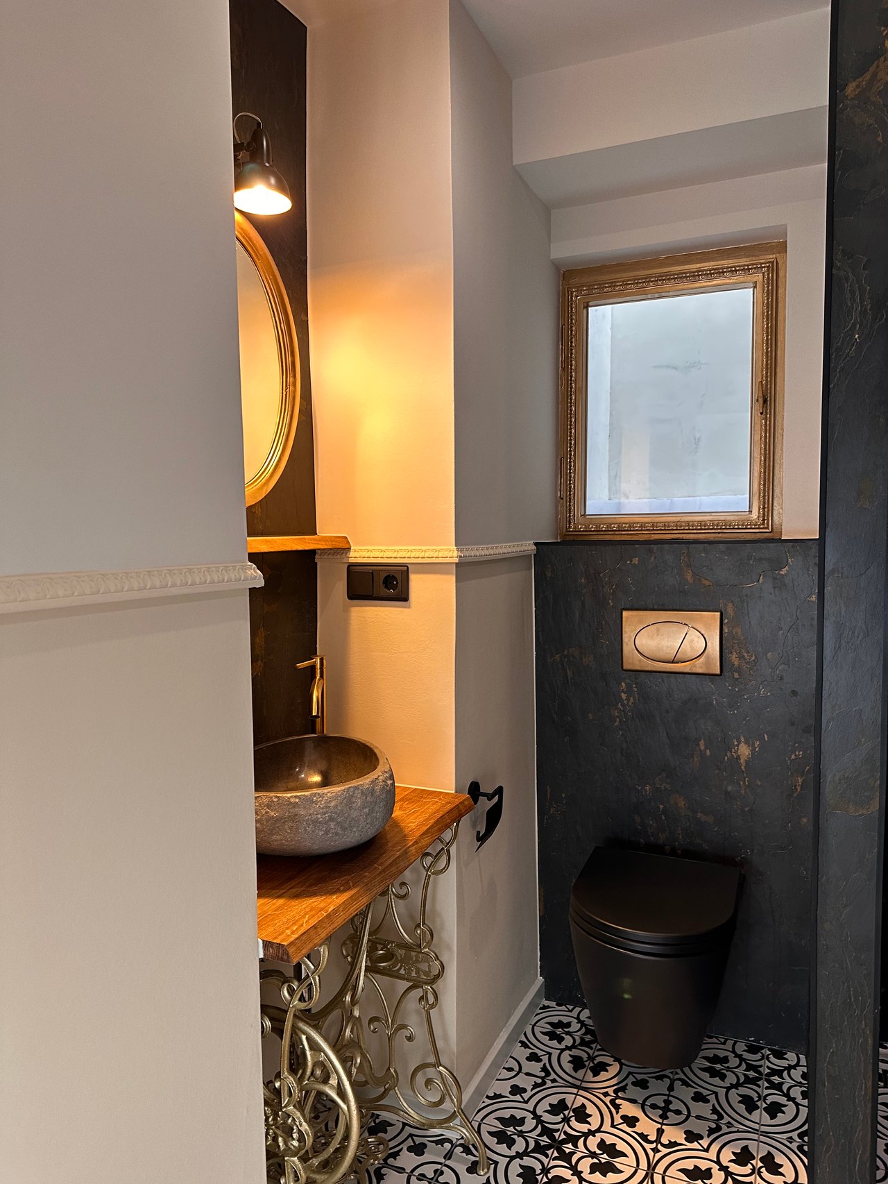 Badezimmer mit Naturstein-Waschtisch, dunkler Wandverkleidung und gemusterten Bodenfliesen