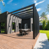 Modernes graues Haus mit Holzterrasse, Pergola und Esstisch im Freien.