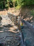 Bau einer Trockenmauer aus Naturstein an einem Hang mit Schotterfundament und Drainageschicht im Garten.