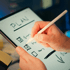 Hände schreiben mit einem Stift auf einem Tablet mit der Überschrift "PLAN" und einer Checkliste.