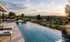 Ein moderner Infinity-Pool auf einer Terrasse mit Sonnenliegen bietet einen weiten Ausblick über eine hügelige Landschaft.