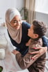 Muslimische Mutter lächelt Sohn an und umarmt ihn. Titel: 150 staatliche Hilfen für Eltern.