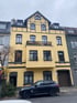 Ein schwarzer SUV parkt vor einem gelben Wohnhaus mit dunklen Fenstern und Dach.