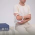 Man sitting, holding a white circular coil around his elbow for PEMF therapy.
