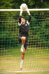 Ein junger Fußballtorwart in schwarzem Trikot und weißen Handschuhen fängt den Ball vor dem Tornetz.